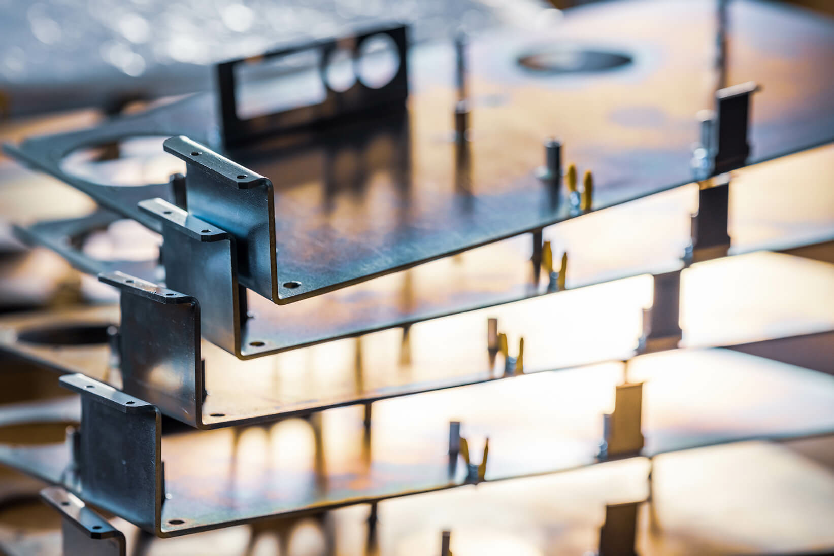 Stack of metal hardware components with bent edges and mounting holes in a factory